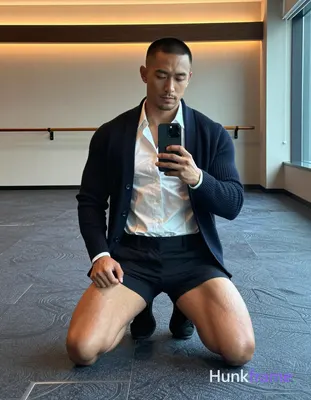A medium-brown skinned man with a black buzz cut and light upper-lip stubble kneels on blue-gray pat