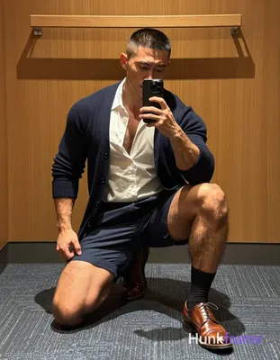 A rugged muscle bear with medium-brown skin and a black buzz cut kneels on blue-