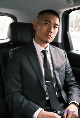 Asian man with buzz cut and light stubble seated upright in a luxury vehicle bac