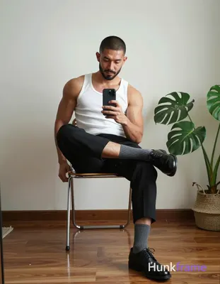 Asian man with short buzz cut and light-medium skin sits on a metal-framed chair, right leg crossed 