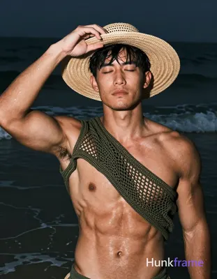 Asian man with tanned skin and short black straight hair stands in shallow water at night, adjusting