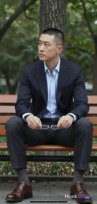 Asian man with short buzz cut and clean-shaven face, neutral contemplative gaze leftward. Seated upr