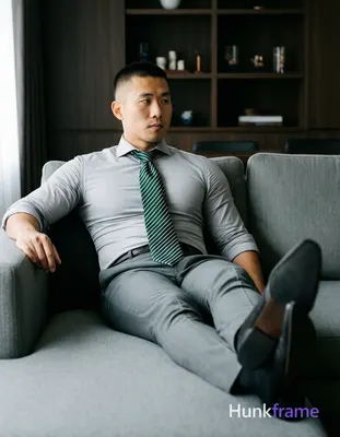 Asian man with short buzz cut and clean-shaven face reclining on a gray sectiona