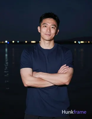 Asian man with short black hair and clean-shaven face stands confidently at a ni