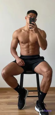 A handsome dark-skinned adult man sits on a black stool in an indoor setting wit