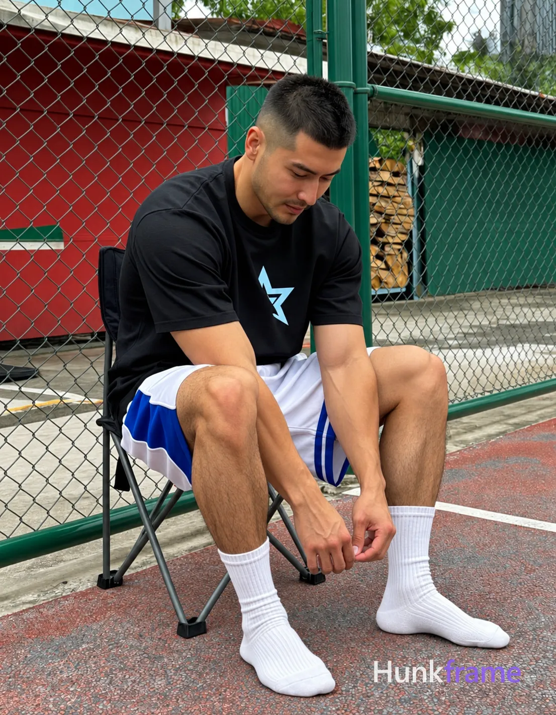 an anonymous figure adult man with short black buzz cut and light stubble on jawline, neutral focused downward gaze; Seated on folding chair outdoors against green chain-link fence, right leg forward adjusting white crew sock with both hands while left hand rests near ankle; Wearing black short-sleeve t-shirt with partially visible light blue star graphic, white basketball shorts with blue side panels mid-thigh waistband; Thick quadriceps and calves defined hamstrings slim waistline fully clothed adult; Natural daylight soft shadows overcast court surface red green stacked firewood background documentary realism sports lifestyle aesthetic, shot on iPhone 15 Pro main camera, authentic smartphone computational photography, natural Smart HDR, vertical 9:16 Xiaohongshu lifestyle post, bright clean gym or cafe scene, wardrobe matching reference outfit, confident everyday blogger pose, phone photo with natural grain; single clean uninterrupted photograph with a cohesive editorial composition and plain continuous surrounding surfaces
