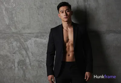 A handsome Asian man with a compact athletic build and well-defined abs, wearing only a black suit j