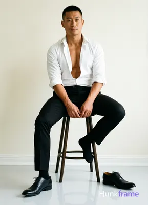 Asian man with short black buzz cut and clean-shaven face, medium-tan skin seated on tall stool in t