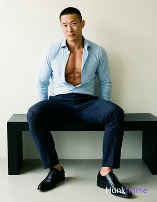Asian adult man with short black buzz cut and clean-shaven face, seated upright on a modern black be