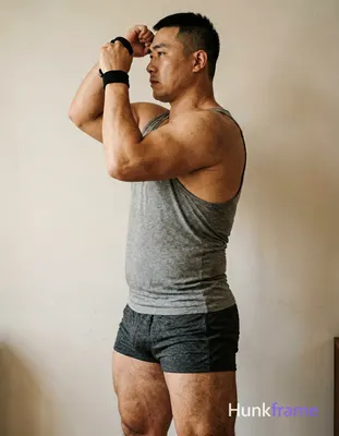 A big hairy stocky masculine man with bear energy, standing in profile with left arm raised behind h