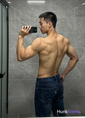 Asian man with short black buzz cut and clean-shaven face, standing sideways facing left in a bathro