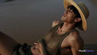 Asian man with tanned skin and short black straight hair reclining diagonally across a beach at dusk
